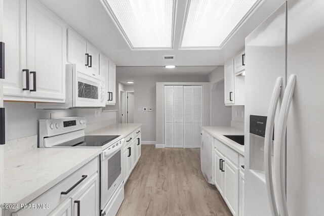 kitchen with white appliances, sink, light stone countertops, light wood-type flooring, and white cabinetry