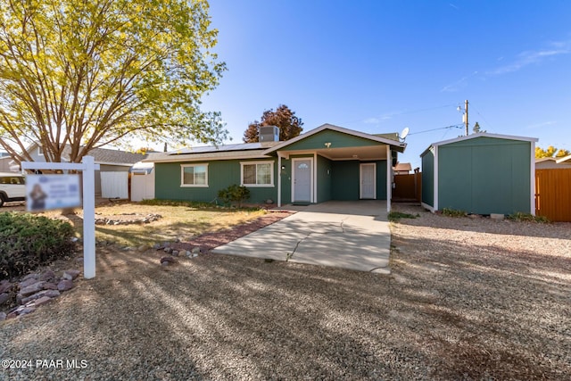 ranch-style home featuring solar panels, a storage unit, and central AC