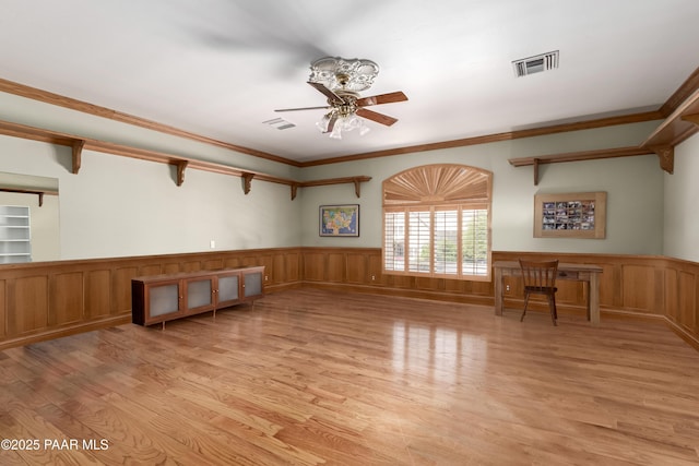 unfurnished living room featuring ceiling fan, a wainscoted wall, light wood-style floors, and visible vents