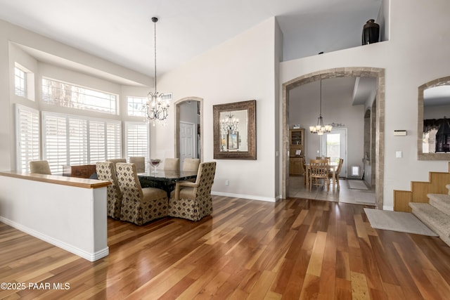 dining room featuring a chandelier, wood finished floors, arched walkways, and high vaulted ceiling