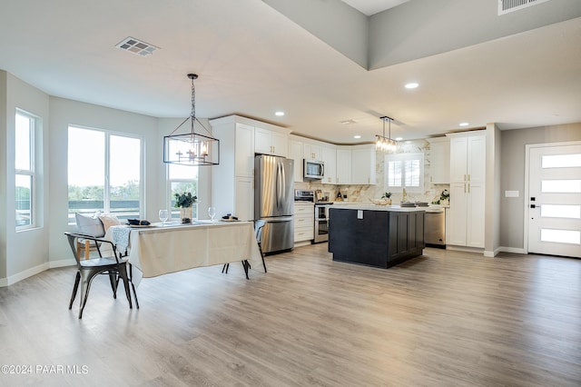 kitchen with light wood-type flooring, decorative light fixtures, a kitchen island, white cabinetry, and stainless steel appliances