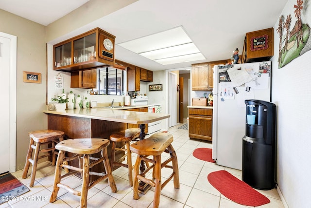 kitchen featuring white appliances, a kitchen breakfast bar, sink, light tile patterned floors, and kitchen peninsula