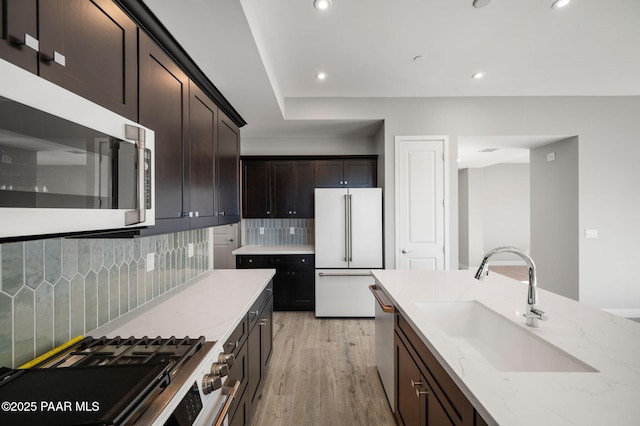 kitchen featuring light stone counters, backsplash, stainless steel appliances, light wood finished floors, and a sink