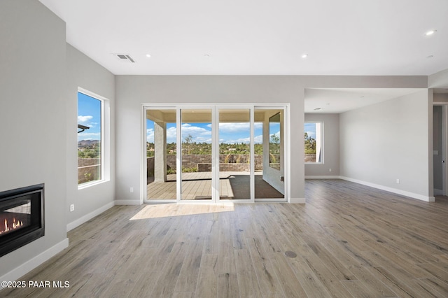 unfurnished living room featuring a wealth of natural light, a glass covered fireplace, visible vents, and wood finished floors