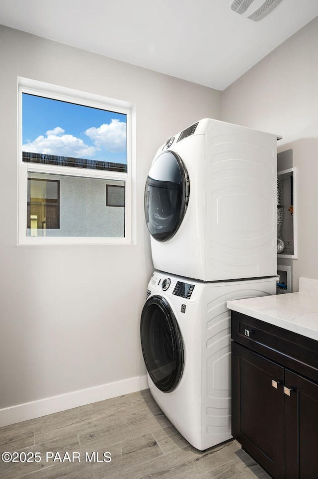 laundry room with stacked washer / dryer, light wood-style floors, visible vents, and cabinet space
