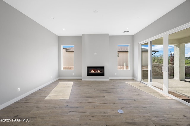 unfurnished living room with wood finished floors, baseboards, a glass covered fireplace, and visible vents