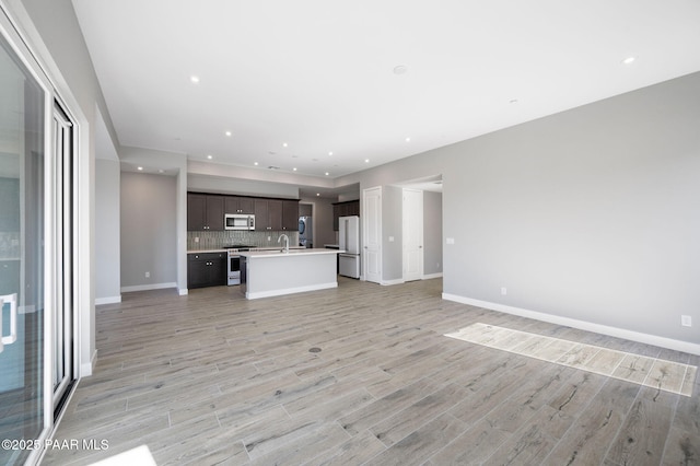 unfurnished living room with a sink, baseboards, light wood finished floors, and recessed lighting