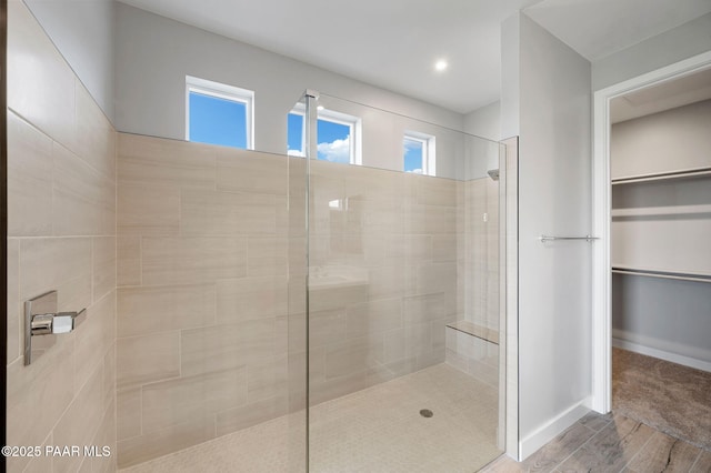 full bathroom with wood finished floors, baseboards, a walk in closet, and walk in shower