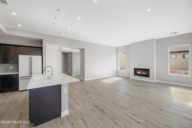 kitchen with white refrigerator, light wood-type flooring, an island with sink, light countertops, and a sink