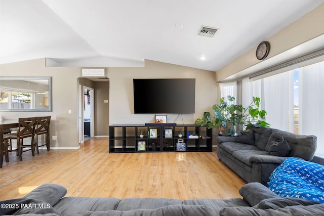 living area with wood finished floors, vaulted ceiling, visible vents, and plenty of natural light