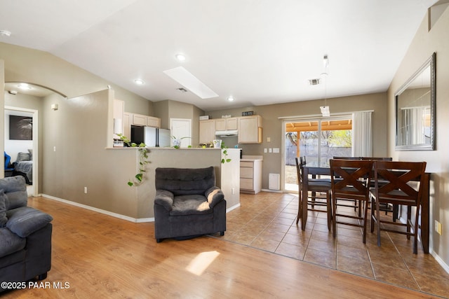 dining area featuring vaulted ceiling with skylight, visible vents, baseboards, and light wood finished floors