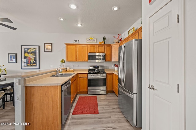 kitchen featuring ceiling fan, sink, stainless steel appliances, kitchen peninsula, and light wood-type flooring