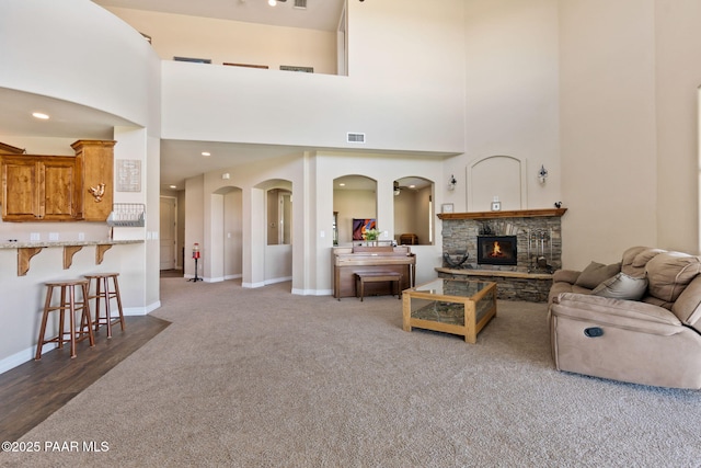 living room featuring a stone fireplace, a towering ceiling, visible vents, baseboards, and carpet flooring