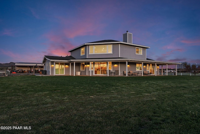 back of property at dusk with a yard, a patio, and a chimney