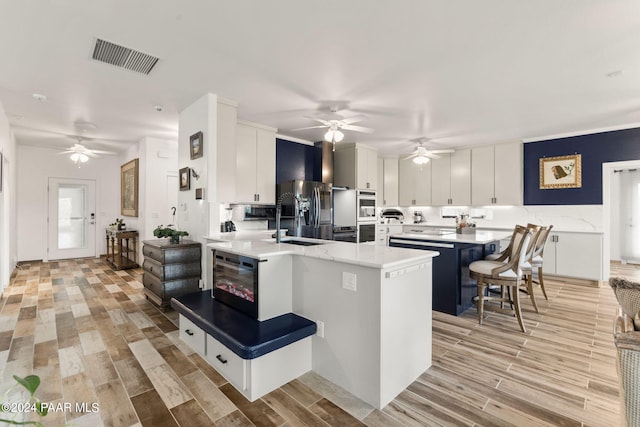 kitchen with a breakfast bar, sink, stainless steel refrigerator with ice dispenser, light hardwood / wood-style flooring, and white cabinetry