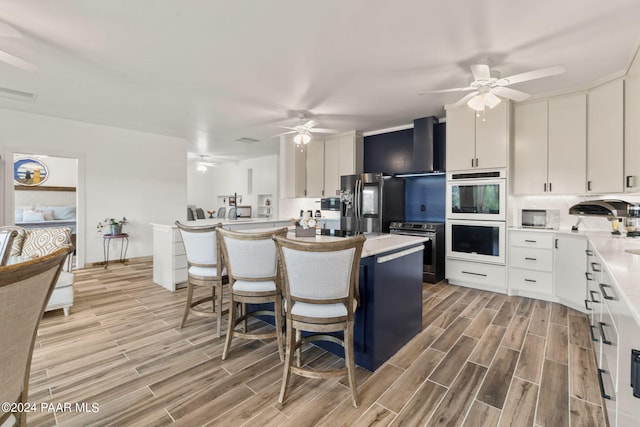 kitchen featuring wall chimney range hood, light hardwood / wood-style floors, a kitchen bar, white cabinetry, and stainless steel appliances