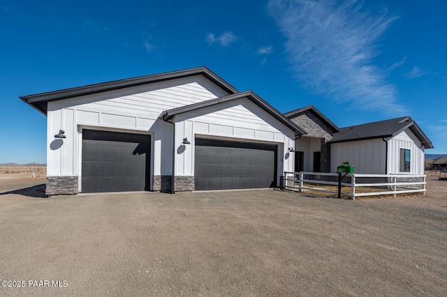 view of front of property featuring an attached garage, fence, stone siding, driveway, and board and batten siding