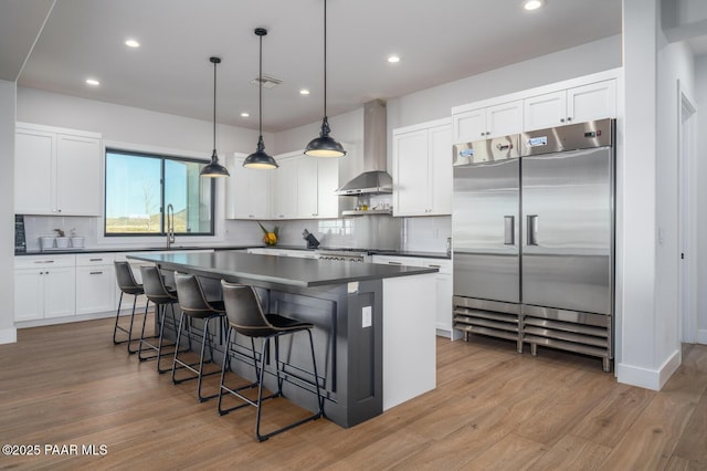 kitchen with stainless steel built in fridge, visible vents, wall chimney range hood, a center island, and dark countertops