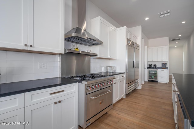 kitchen with wine cooler, dark countertops, visible vents, high quality appliances, and wall chimney exhaust hood