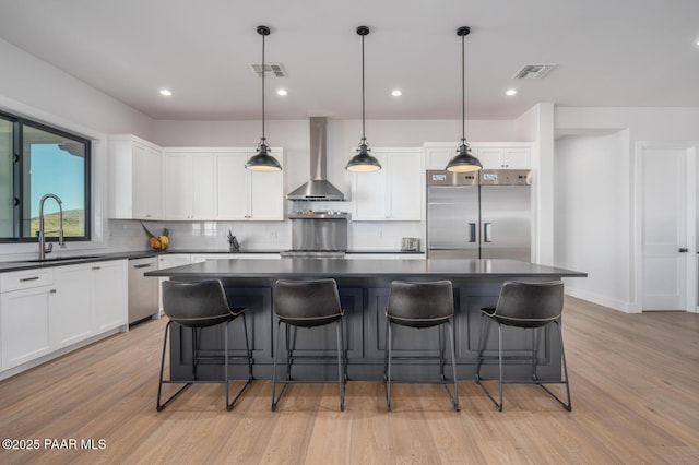 kitchen with appliances with stainless steel finishes, dark countertops, a sink, and wall chimney range hood