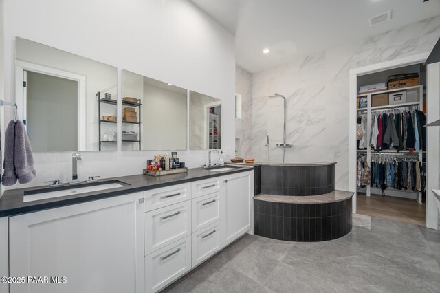 bathroom with a spacious closet, double vanity, a sink, and visible vents