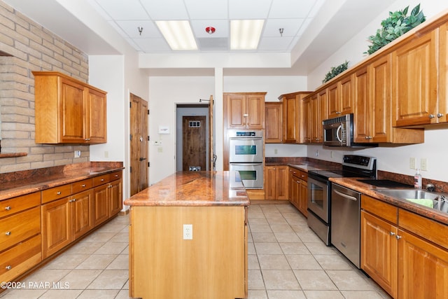 kitchen featuring a center island, brown cabinets, appliances with stainless steel finishes, dark stone countertops, and light tile patterned flooring