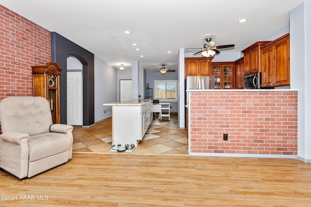 kitchen with brick wall, glass insert cabinets, appliances with stainless steel finishes, brown cabinetry, and a ceiling fan