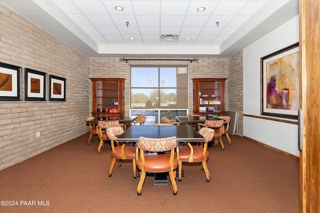 carpeted dining space with a drop ceiling, visible vents, baseboards, and brick wall