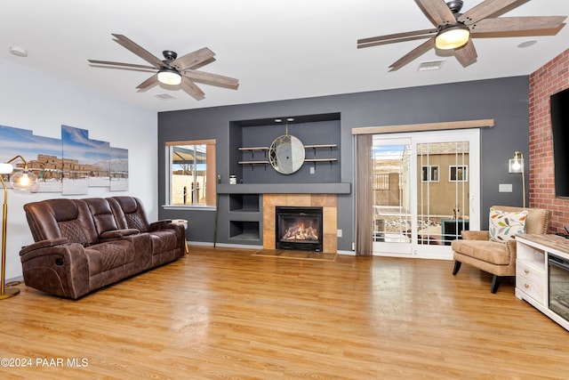 living area featuring a tiled fireplace, visible vents, light wood-style flooring, and ceiling fan