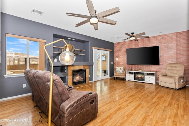 living room featuring a ceiling fan, wood finished floors, visible vents, baseboards, and a glass covered fireplace