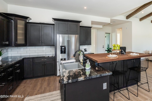 kitchen with beam ceiling, sink, light wood-type flooring, and a kitchen island with sink