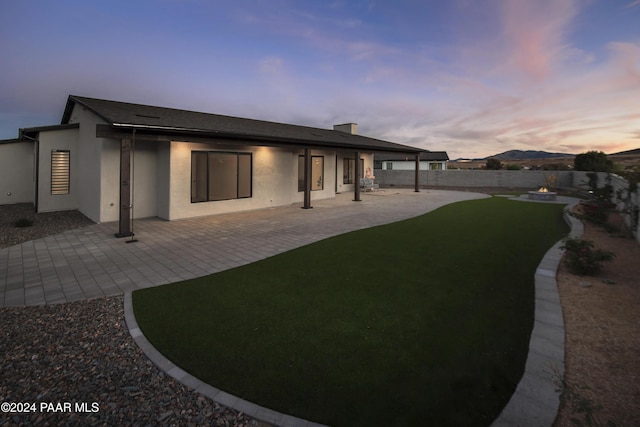 back house at dusk with a patio area and a lawn