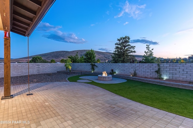 patio terrace at dusk featuring a lawn, a mountain view, and an outdoor fire pit