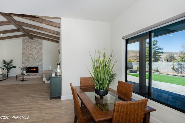 dining space with lofted ceiling with beams, a fireplace, and light hardwood / wood-style flooring