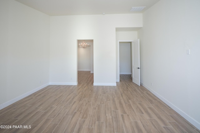 spare room with light wood-type flooring and an inviting chandelier