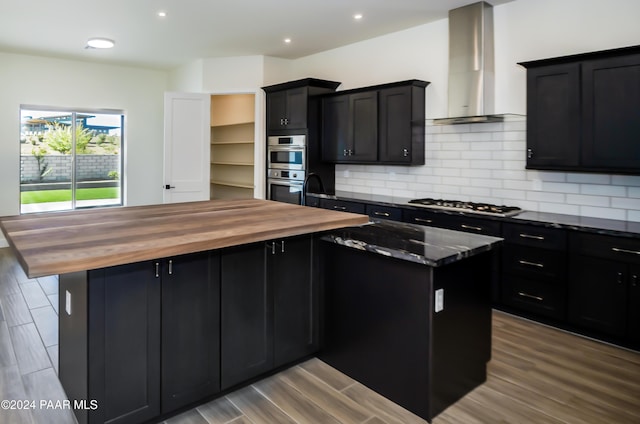 kitchen with light hardwood / wood-style floors, a center island, wall chimney range hood, and stainless steel appliances