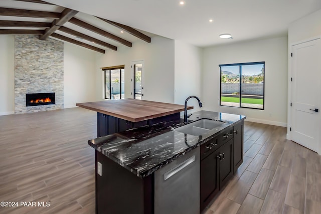 kitchen featuring a kitchen island with sink, sink, dark stone counters, and light hardwood / wood-style flooring