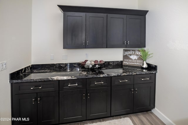 bar with light wood-type flooring and dark stone counters