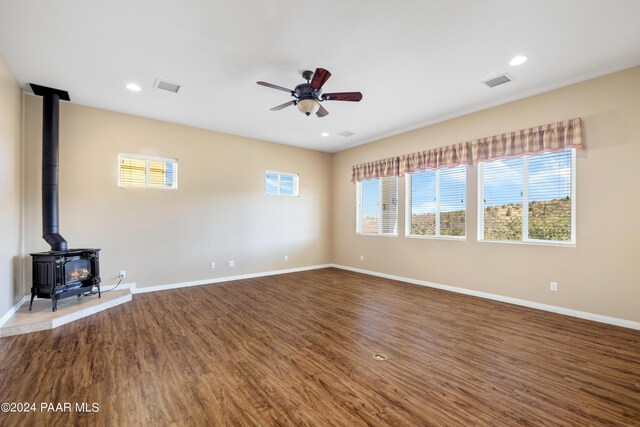 unfurnished living room featuring wood-type flooring, a wood stove, and ceiling fan