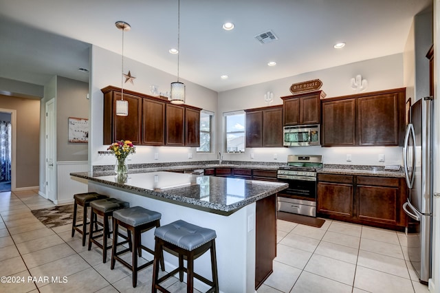 kitchen featuring a breakfast bar, a center island, dark stone countertops, decorative light fixtures, and stainless steel appliances