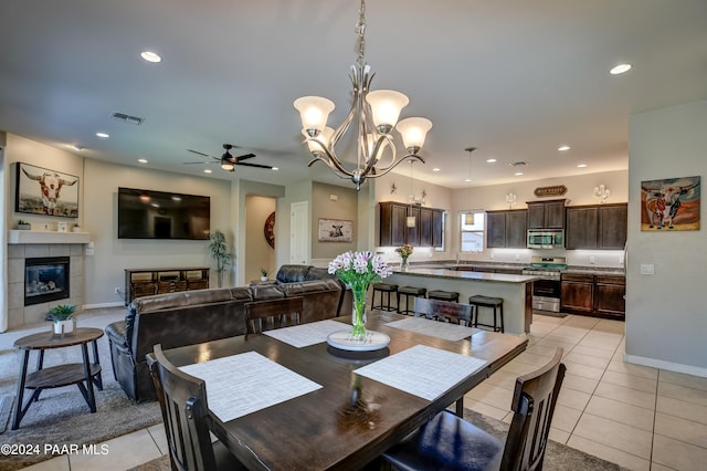 tiled dining area featuring ceiling fan with notable chandelier and a tiled fireplace