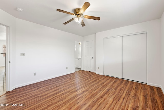 unfurnished bedroom with a ceiling fan, wood finished floors, baseboards, a closet, and ensuite bathroom