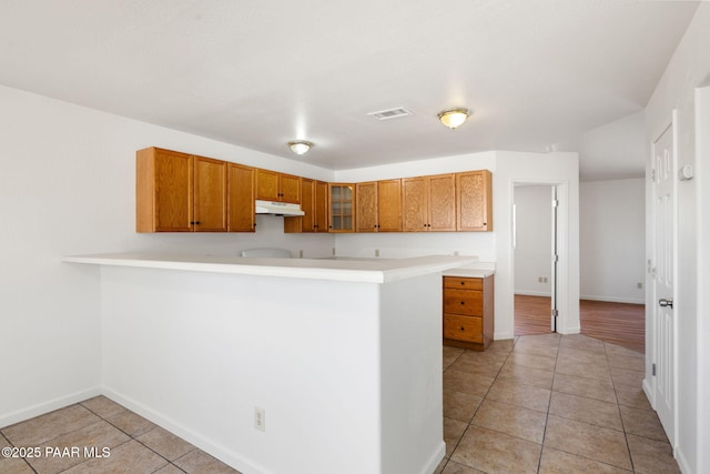 kitchen featuring under cabinet range hood, a peninsula, light countertops, and light tile patterned flooring