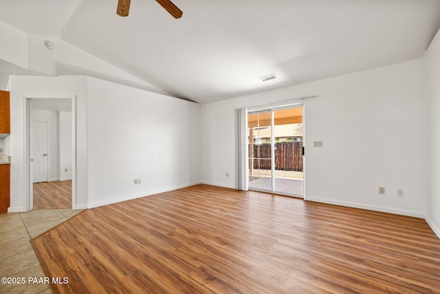 empty room featuring light wood finished floors, visible vents, baseboards, ceiling fan, and vaulted ceiling