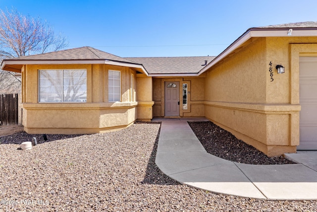 entrance to property featuring stucco siding, fence, a garage, and a shingled roof