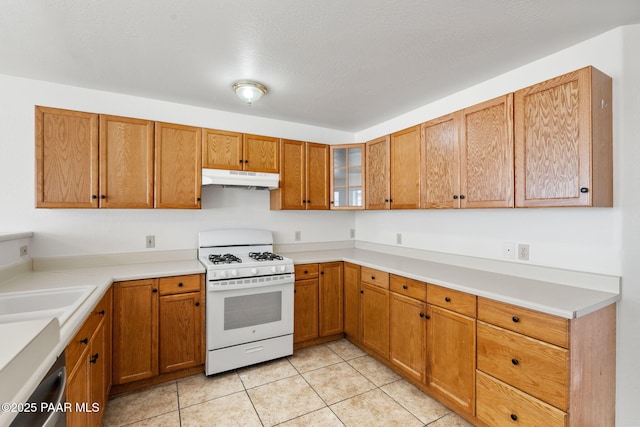 kitchen with brown cabinets, under cabinet range hood, light tile patterned floors, glass insert cabinets, and white gas range