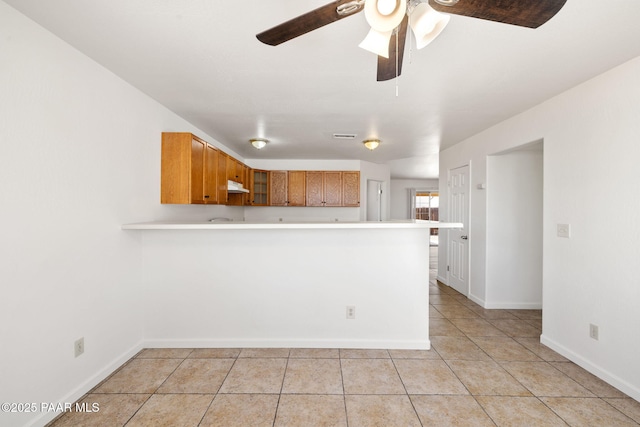 kitchen featuring glass insert cabinets, light countertops, light tile patterned floors, brown cabinets, and a peninsula