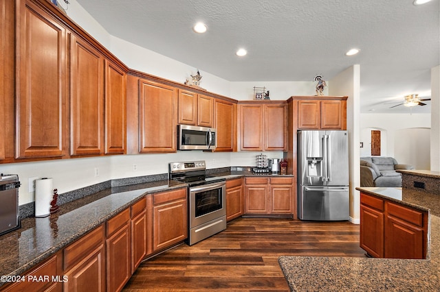 kitchen with dark stone counters, dark hardwood / wood-style floors, ceiling fan, a textured ceiling, and stainless steel appliances