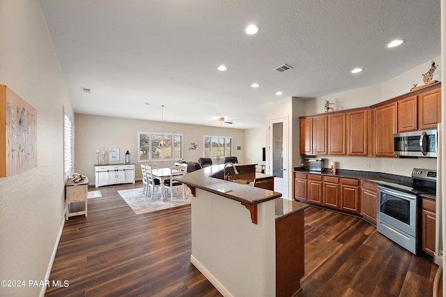 kitchen with a kitchen bar, appliances with stainless steel finishes, dark hardwood / wood-style flooring, a kitchen island with sink, and hanging light fixtures