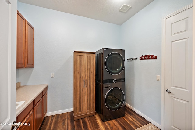 laundry room featuring cabinets, dark hardwood / wood-style floors, and stacked washer / drying machine